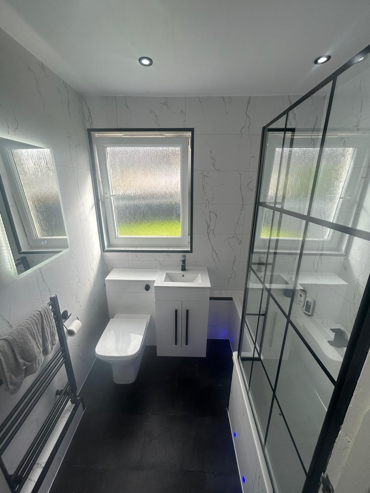 White marble-effect bathroom with a black-framed bath screen and black fittings