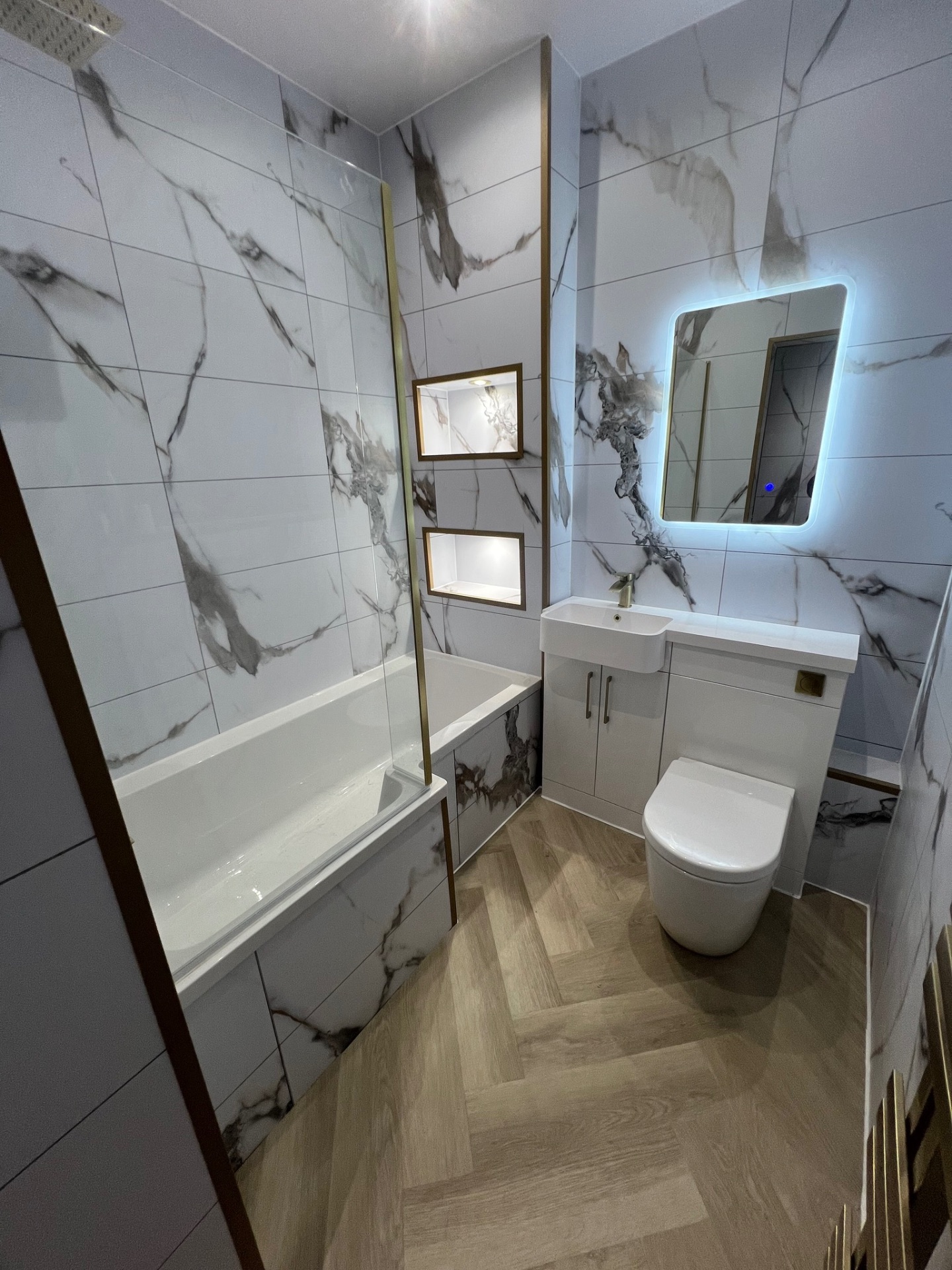 Marble-effect bath suite with brass-coloured trim and illuminated wall recesses
